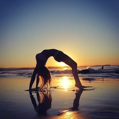 A person doing a backbend on a wet beach at sunset
