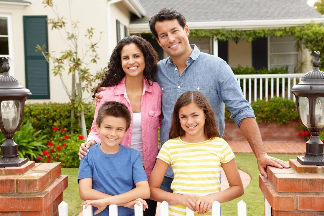 A smiling family of four outside a house