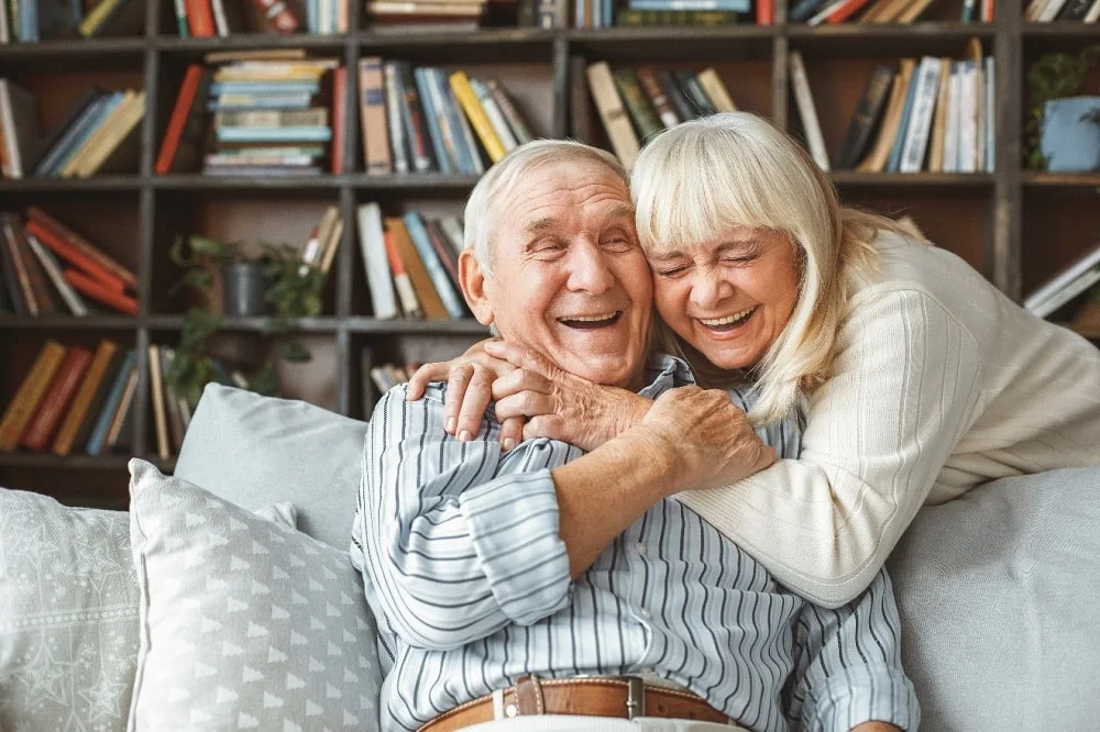 An older couple laughing and embracing on a sofa